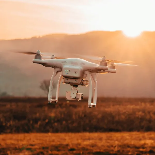 3 drone flying against a brightly lit backdrop of a rising sun over a field